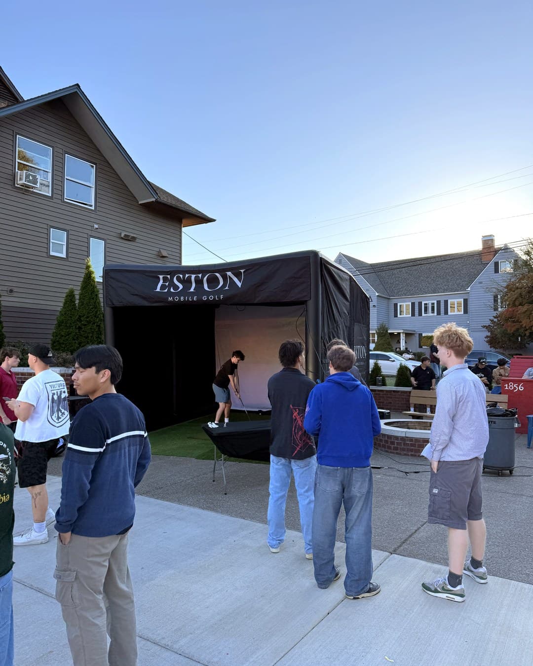 Guests gathered outside the lit enclosure at an evening event, watching a player take a shot.