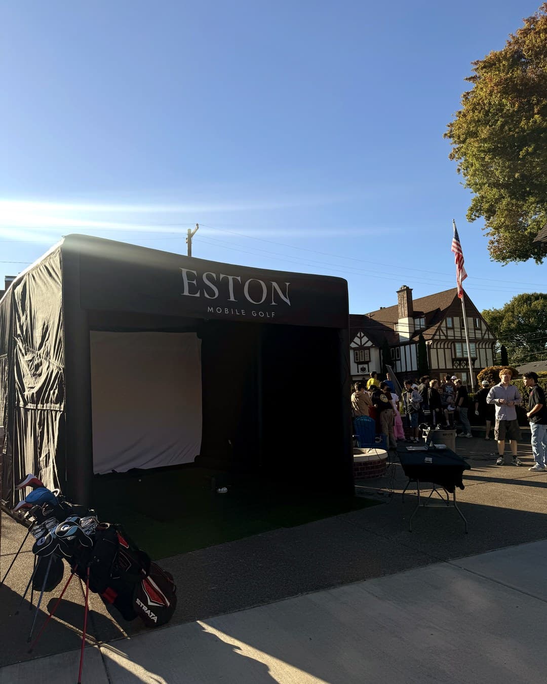 The Eston Mobile Golf enclosure set up outdoors on a driveway in daylight, with club bags standing in the foreground.